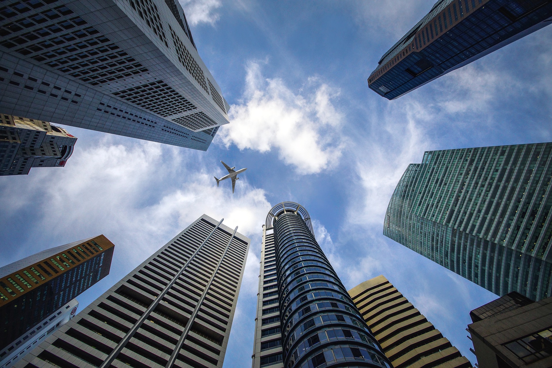 looking up at the sky at a plane passing over singapore skyscrapers