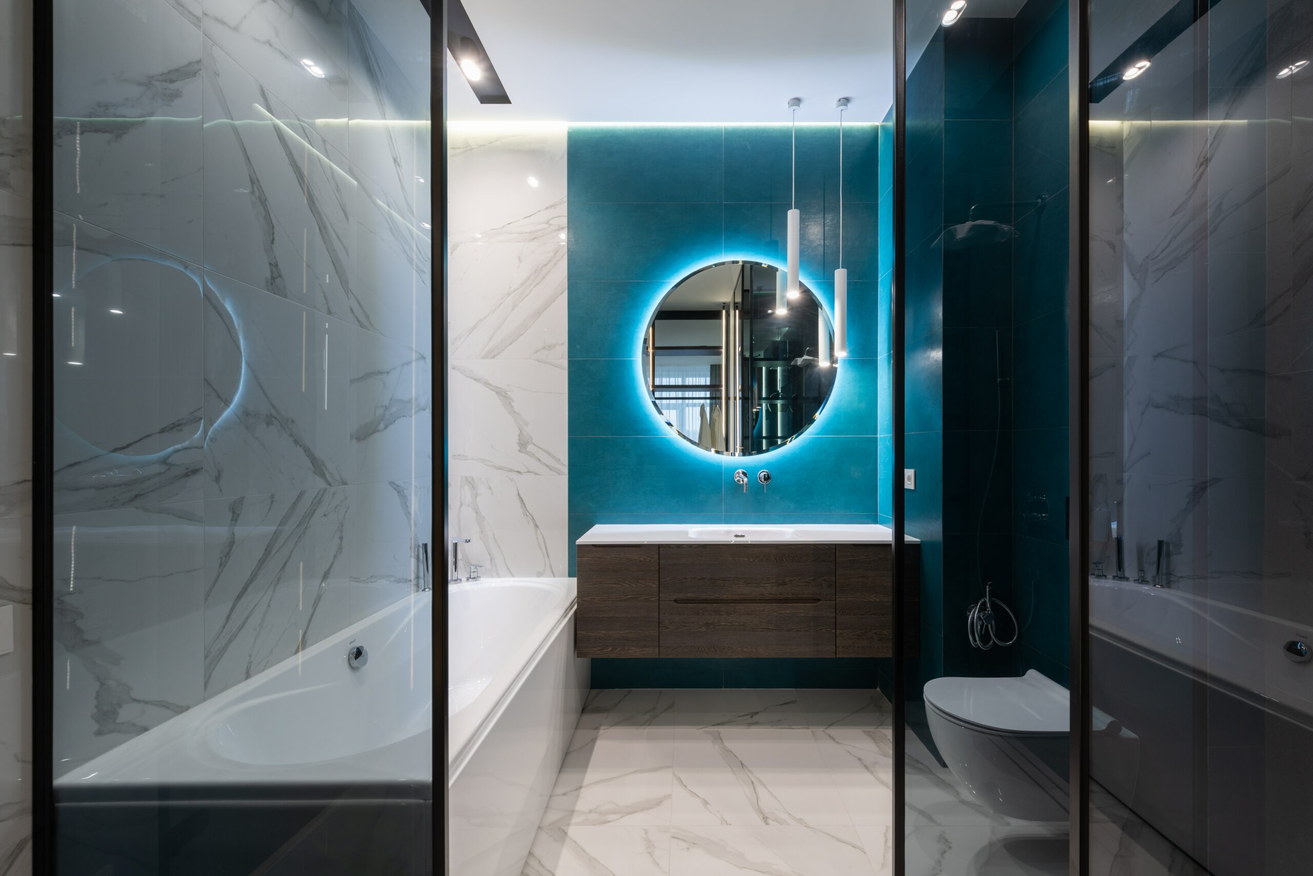 modern bathroom with a blue accent wall and lighted circle mirror