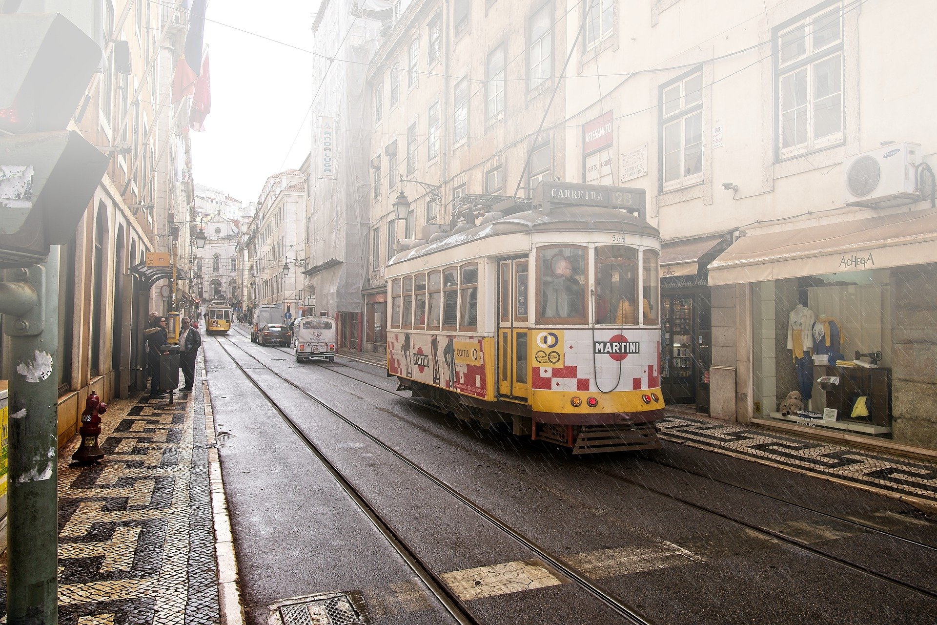 yellow tram going down a street lined with shops in lisbon, portugal