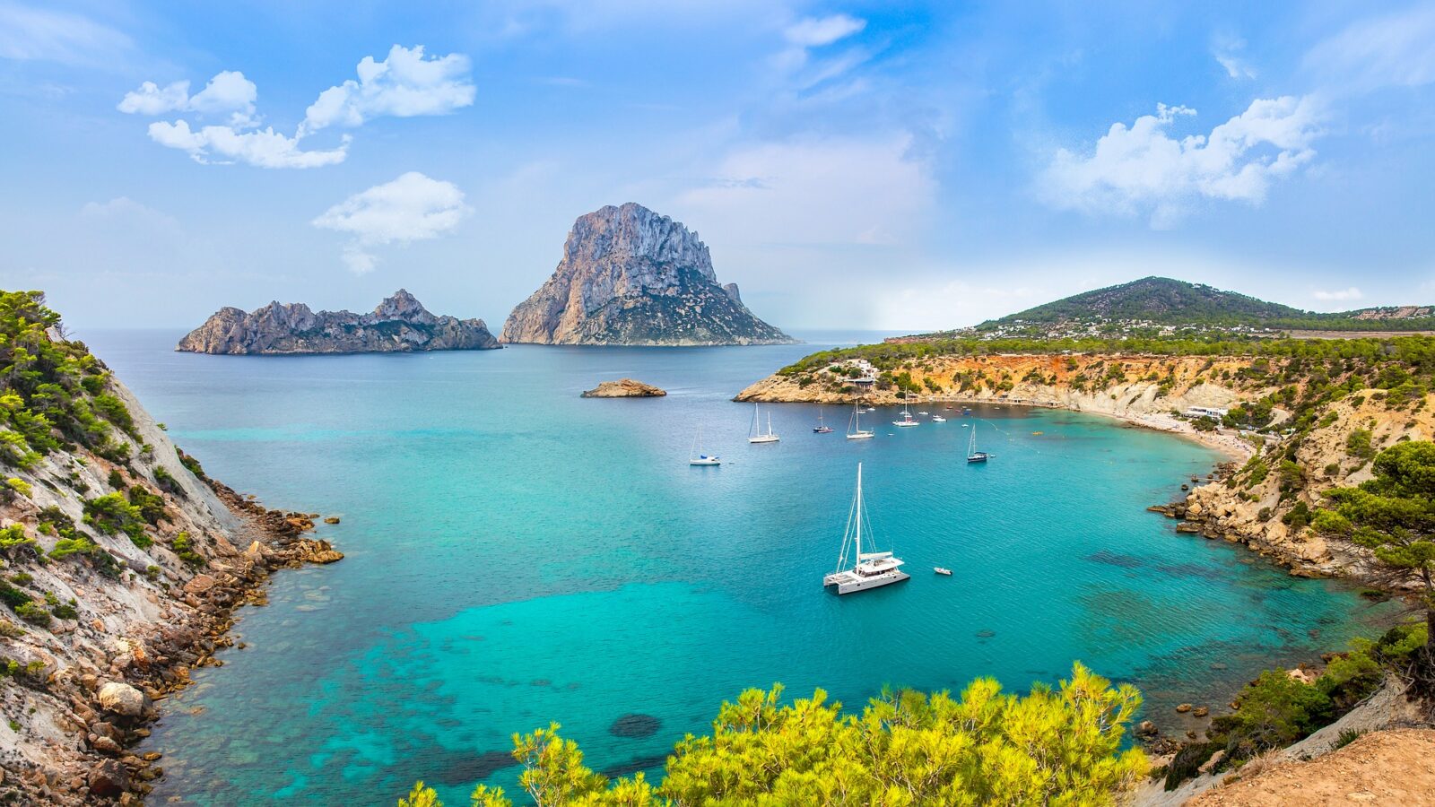 turquoise ocean cove in ibiza, spain with boats and an island in the background