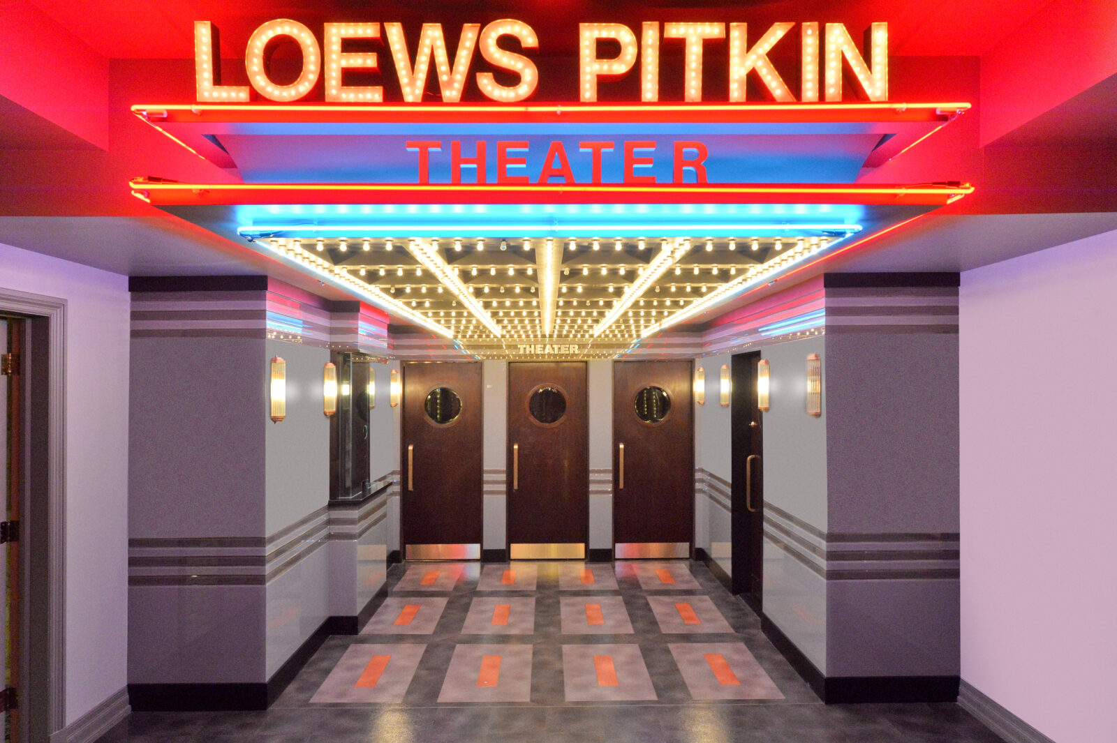 A wide hallway with Theater doors under a bright theater sign.