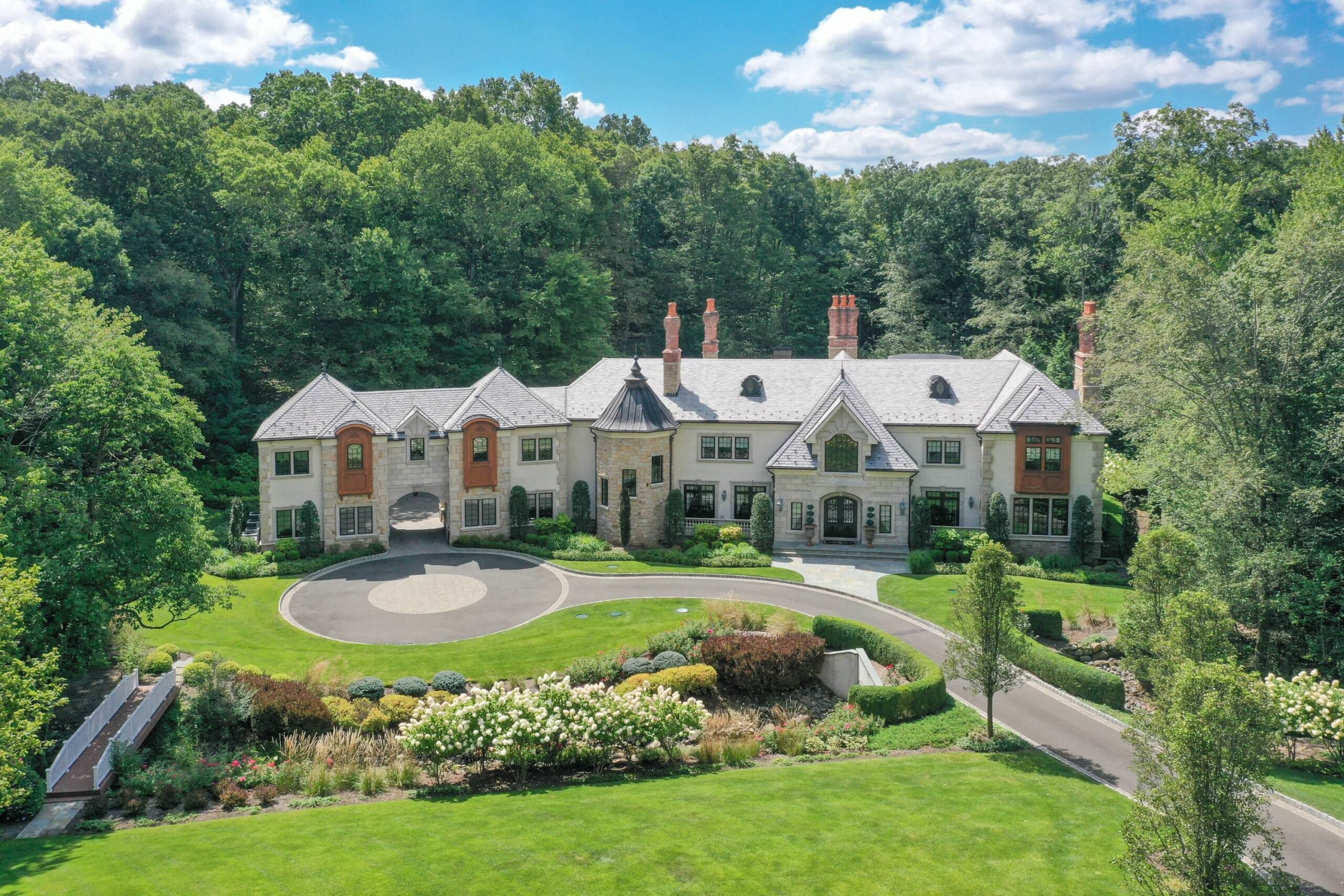 A large building with a long driveway. There's a river in front of it and tall trees behind it.