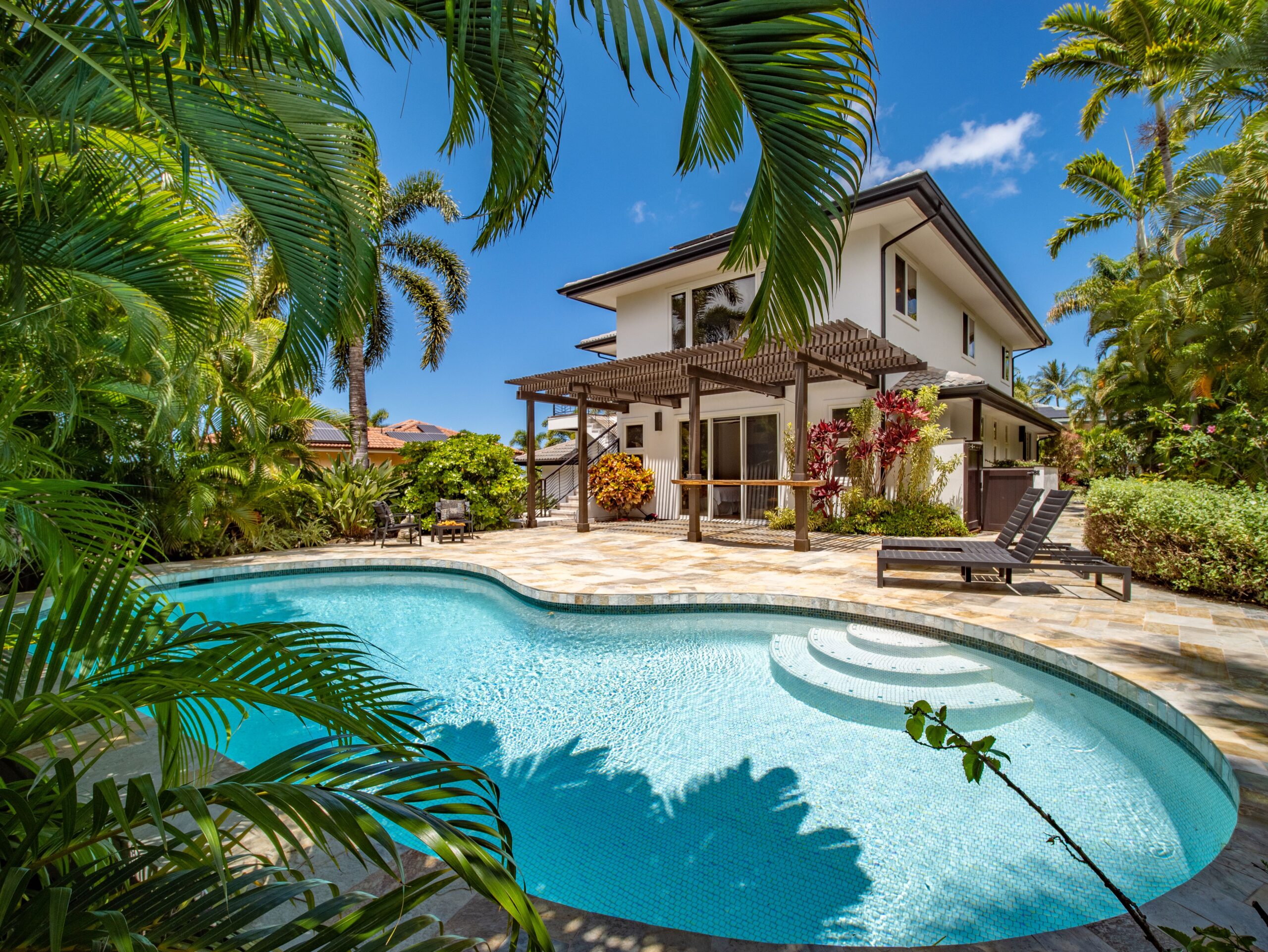 A clear blue pool in front of a concrete walled tropical property.