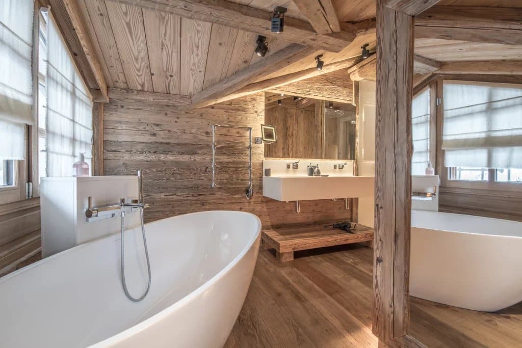 The bathroom of a chalet covered with wood floors and walls and a bathtub.
