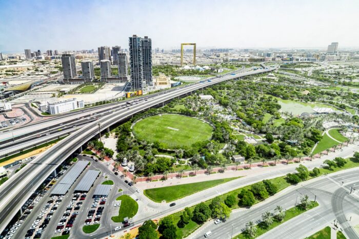 An overhead view of fields and trees in Dubai, connected to a highway and tall buildings.