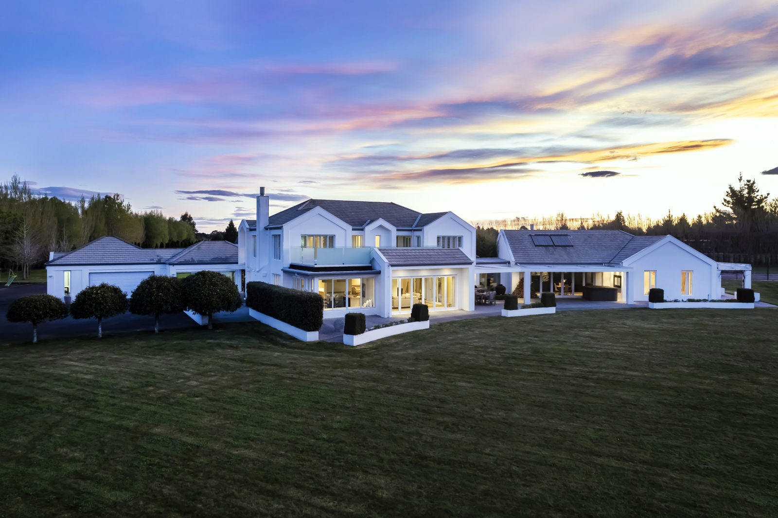 An expansive white house adorned with trees, hedges, and a vast lawn.