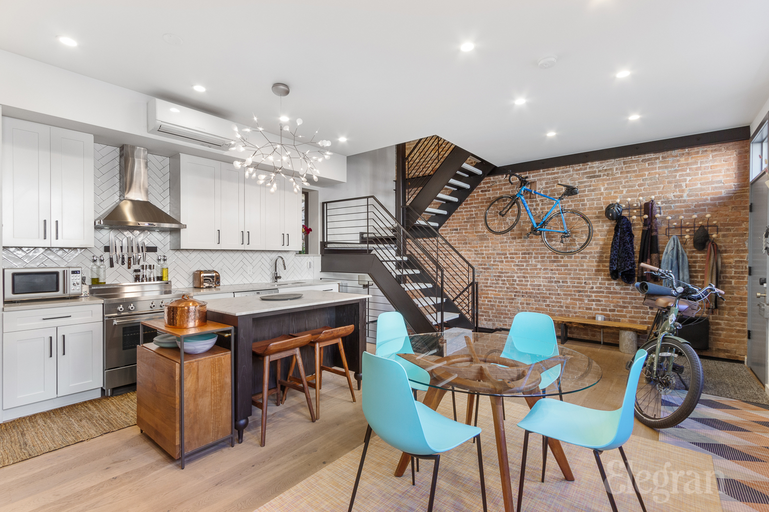 a dining and kitchen area with stairs and a brick wall with a bike hanging on it.