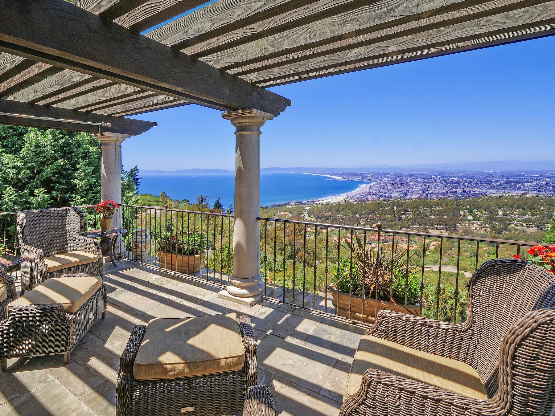 An outdoor sitting area with wicker chairs with a view of the ocean and a distant town.