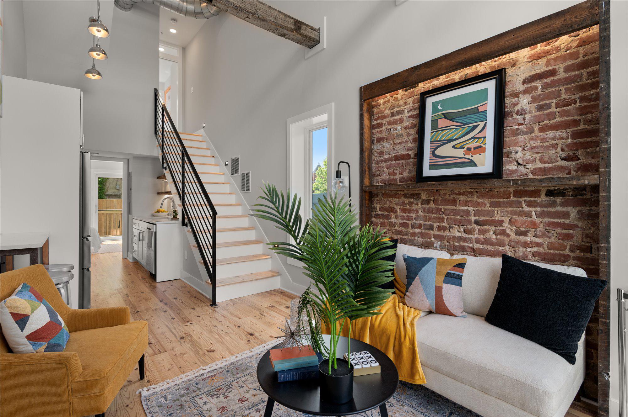 A lobby with white walls, one rustic brick wall, a fridge, and a stairway.