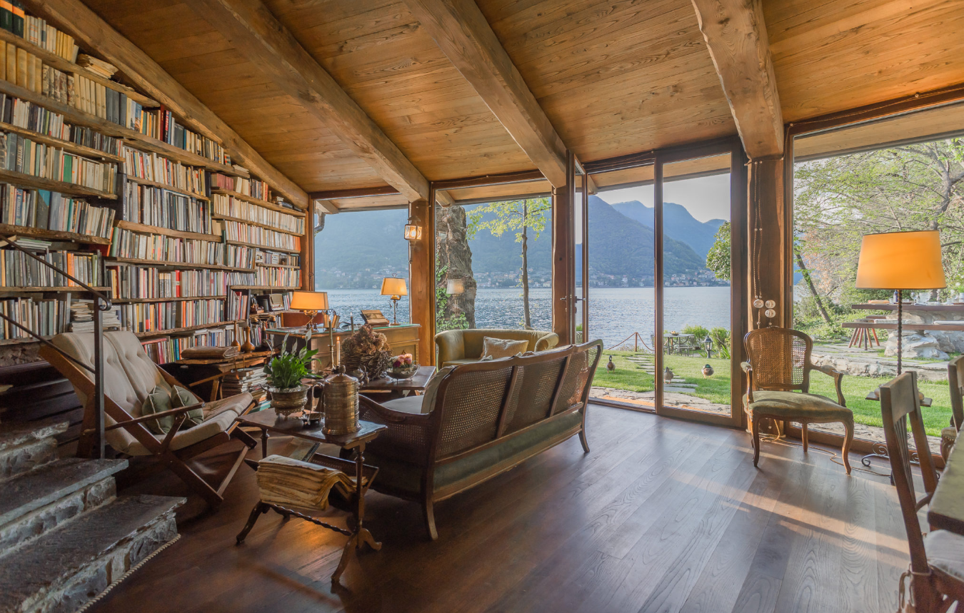 A rustic library with wicker furniture and a view of a lake.
