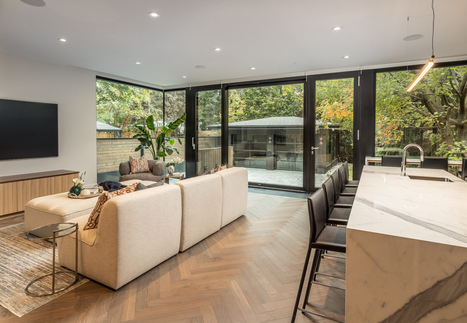 A living area with a sitting area, kitchen island, and TV, all on a herringbone floor.