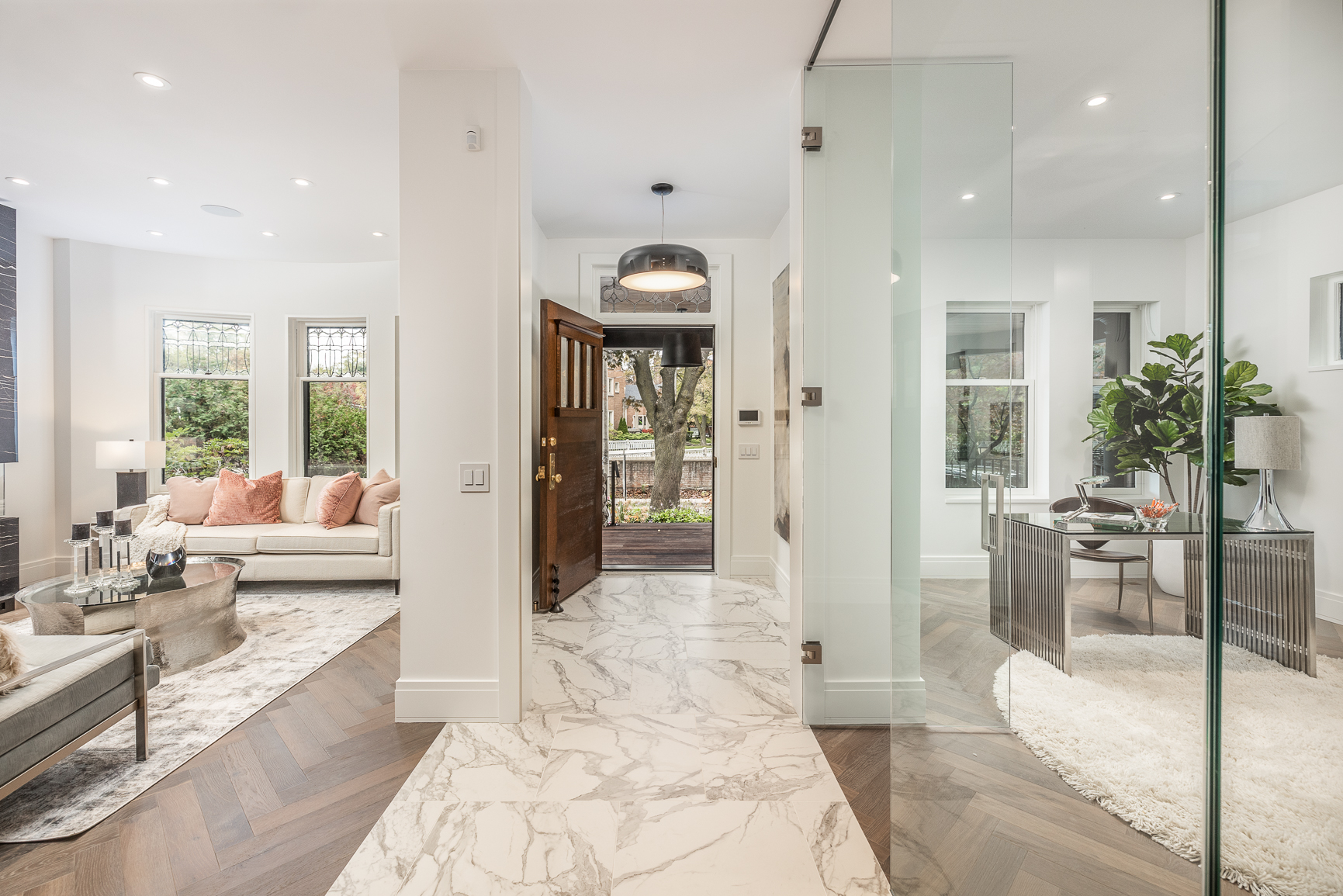 A home entrance and living room with white furniture on a herringbone floor.