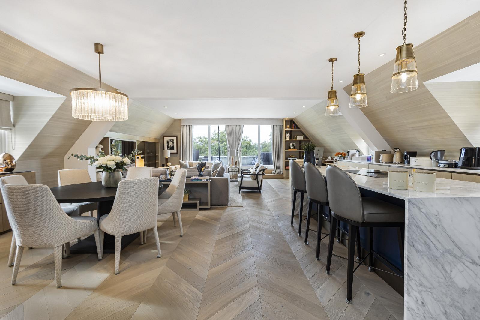 A wide room with tables and a kitchen counter atop a herringbone floor.
