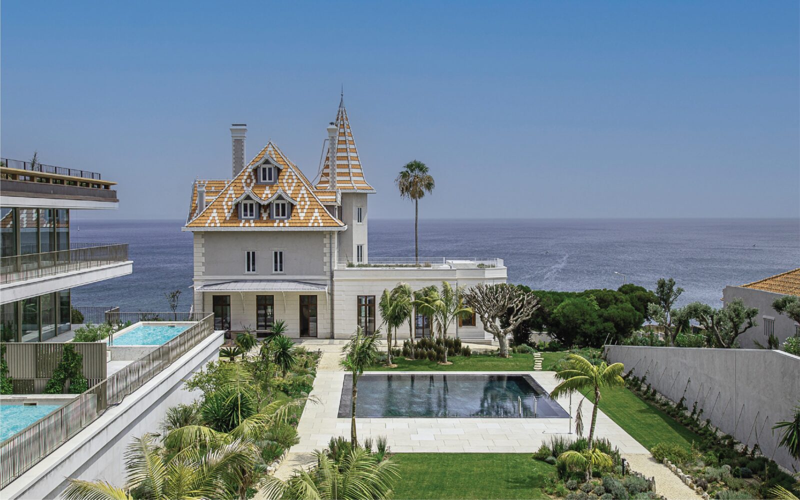 An house by a body of water with a pool and a golden roof and spires.