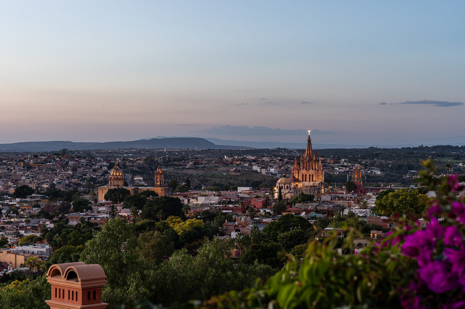 A distant view of a city with cathedrals. Mountains are in the background.