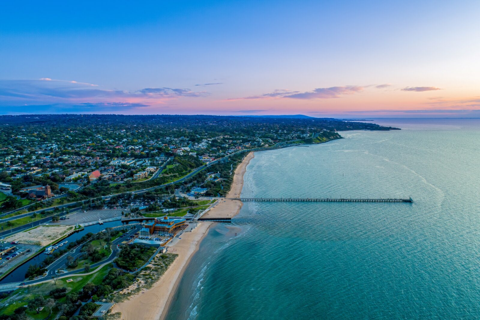 A skyview of a plot of land with a shoreline and a dock with buildings in the background.