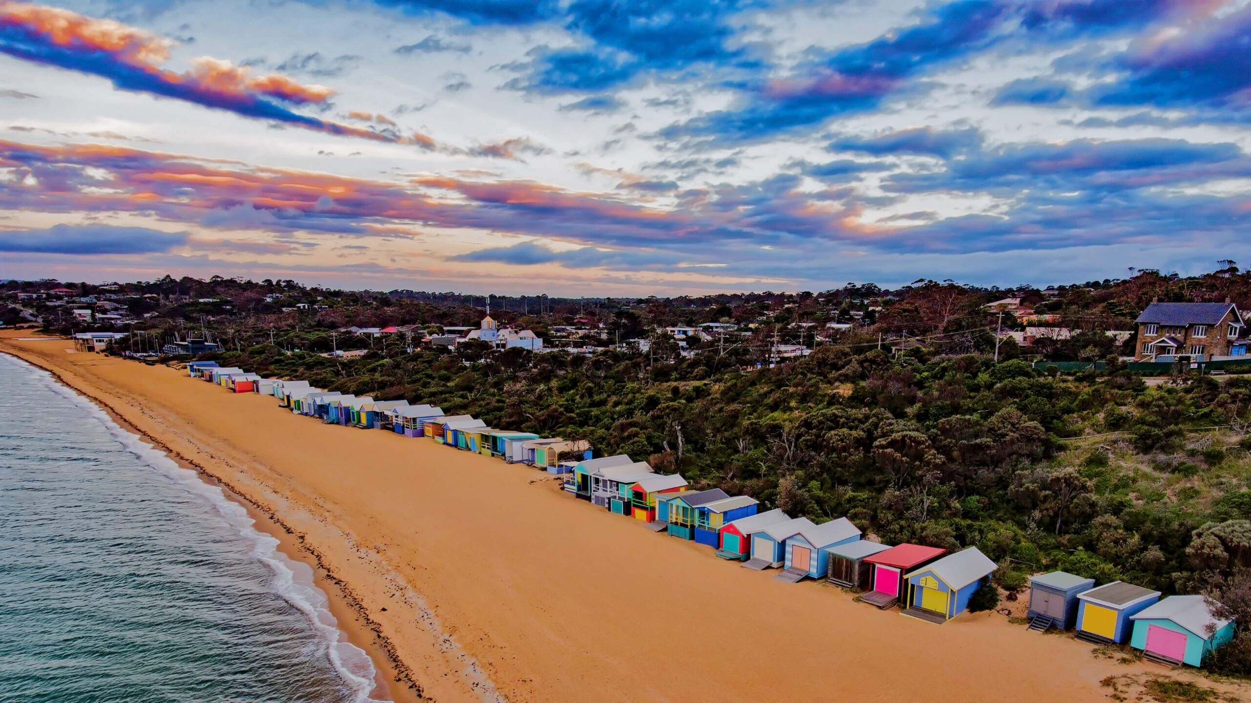 A shoreline with a collection of colorful beachboxes lining it.