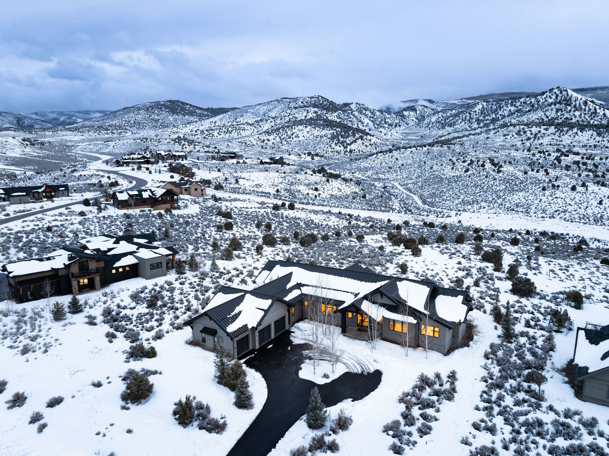 A collection of homes on a snowy hilly landscape with lots of trees.