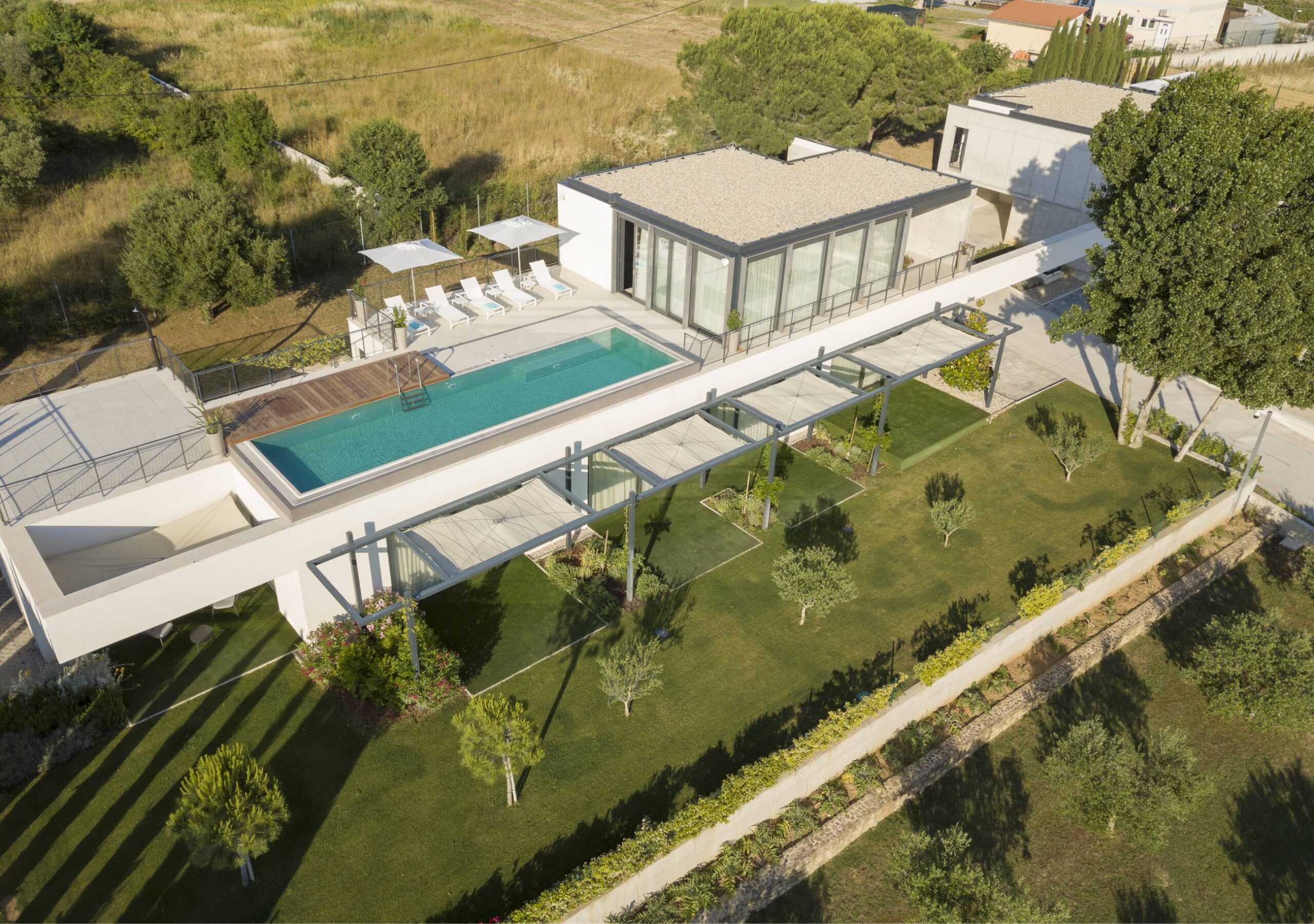 An aerial view of a square contemporary house with a green yard and a pool.