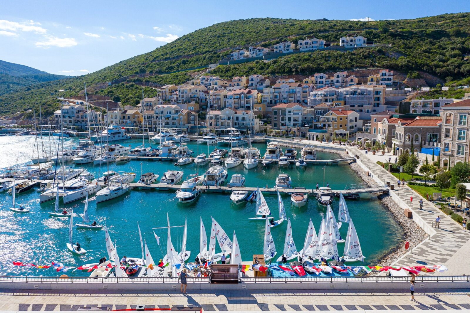 A harbor filled with boats surrounded by a town on a big green hill.