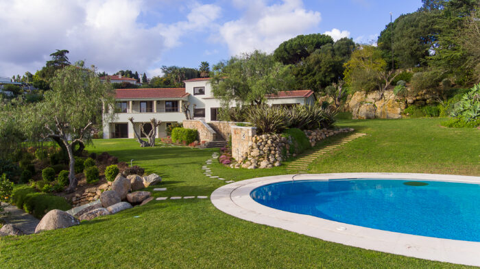 A villa with a red roof, a green yard, and a clear blue pool.