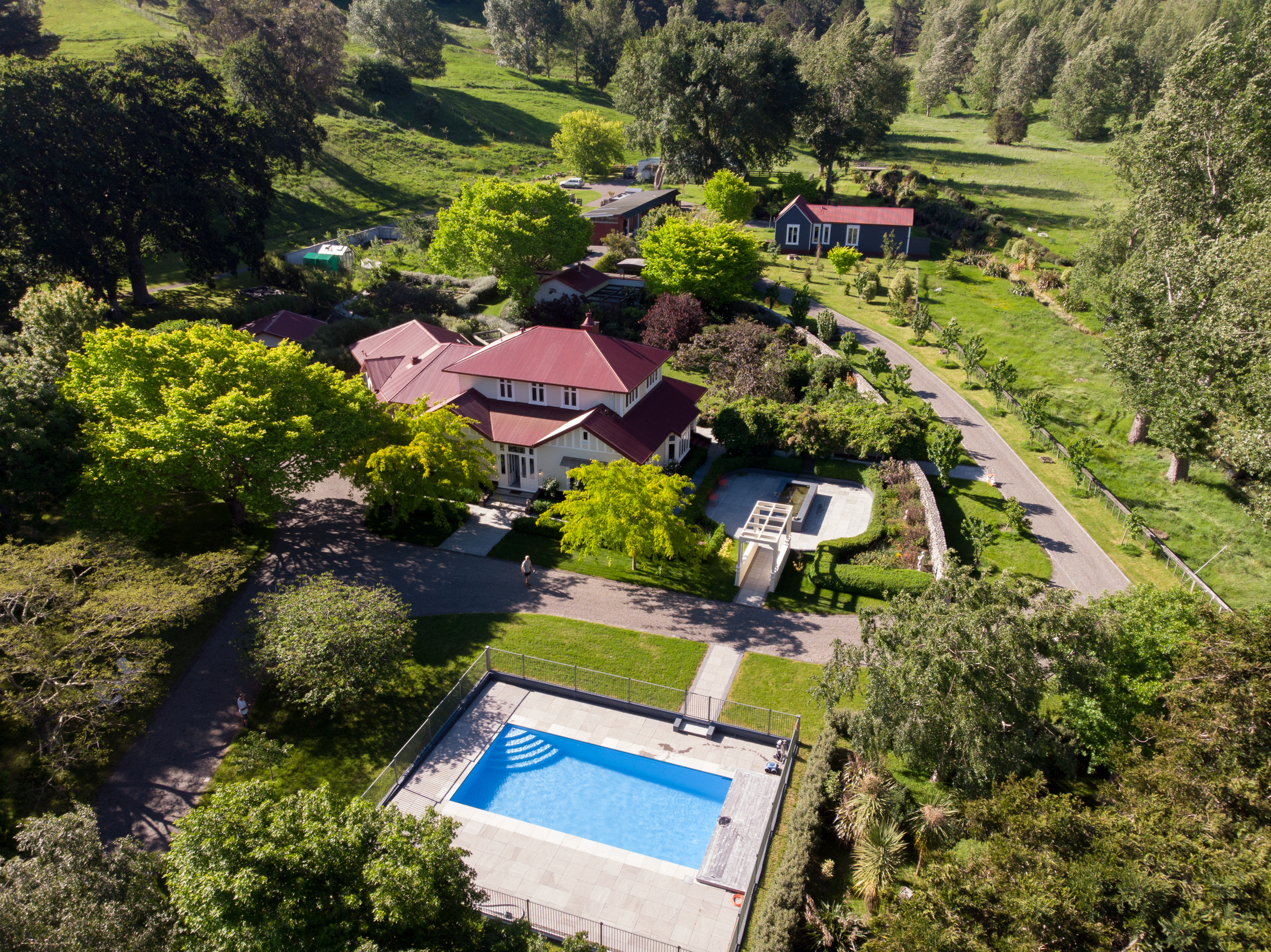 A big house with a red roof and a pool surrounded by trees.