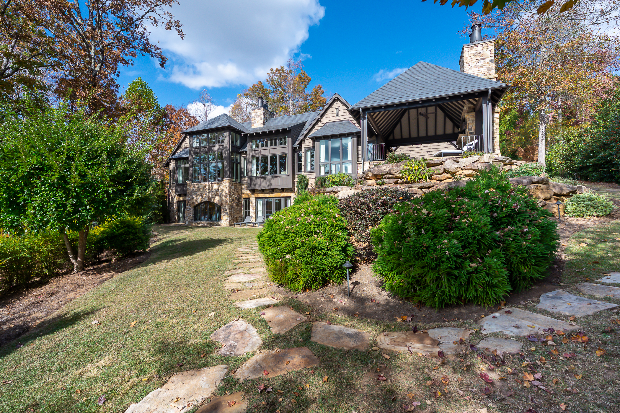 A big house with green bushes in front of it and a stone trail that surrounds it.