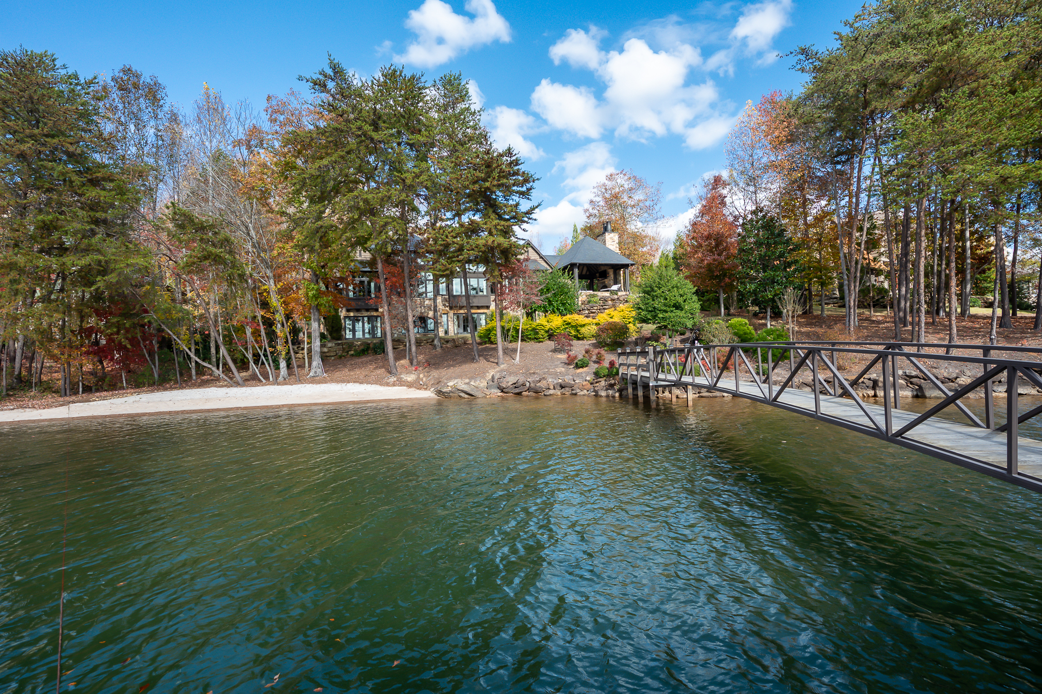 A body of water with a bridge going over it and a large estate behind a row of trees.