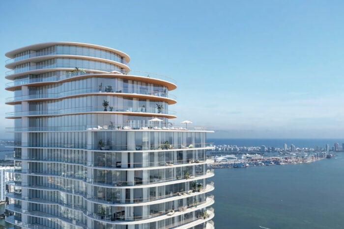 A high rise glass building with a view of the ocean and a peninsula behind it.
