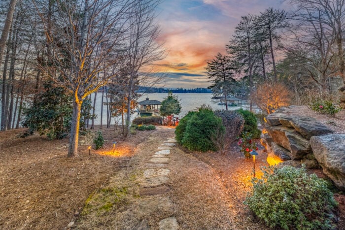 A stone trail leading to a gazebo on the water with trees on both sides.
