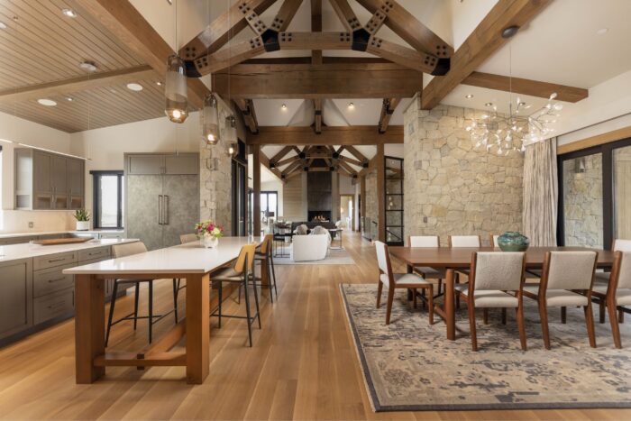 Open-concept living area in modern mountain estate with timber trusses and limestone walls. 