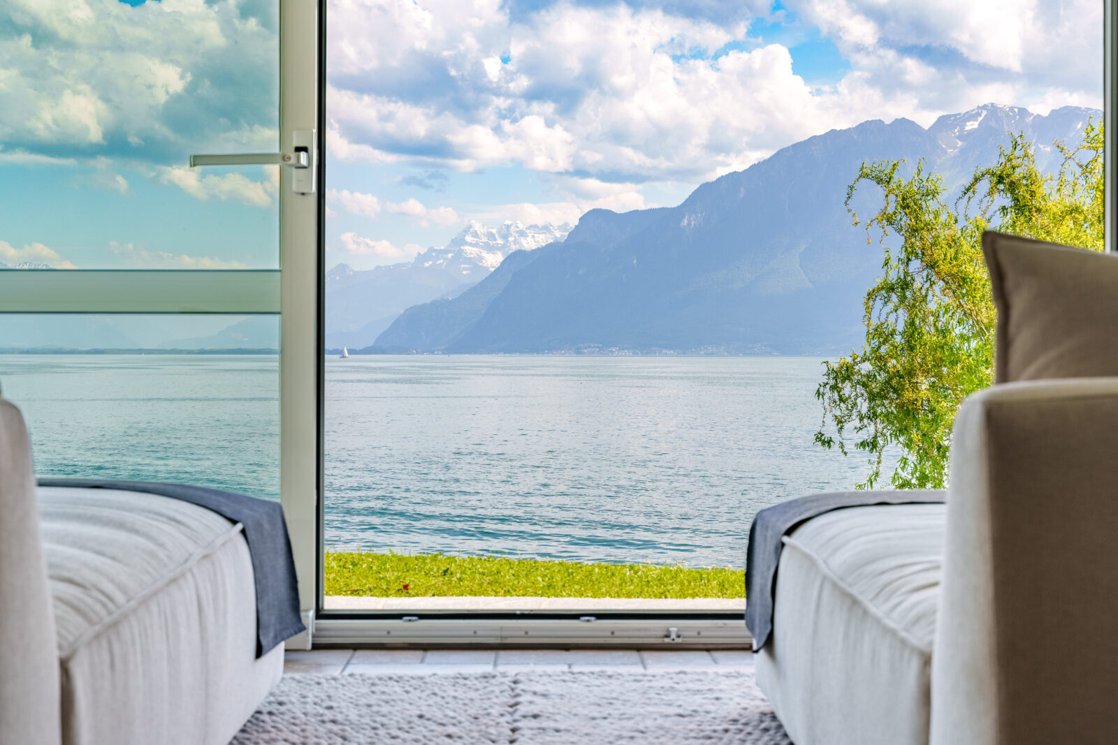 Floor-to-ceiling windows open a bedroom to a view of Lake Geneva and mountains beyond. 