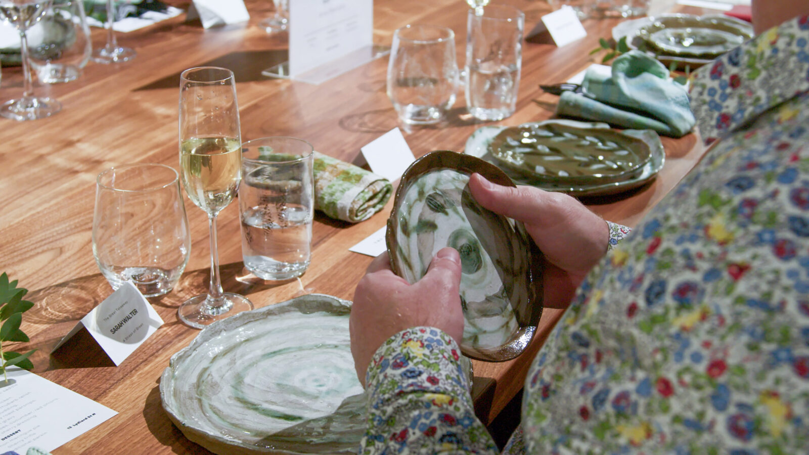 Crop of female hands holding a hand-made dinner plate at a set table