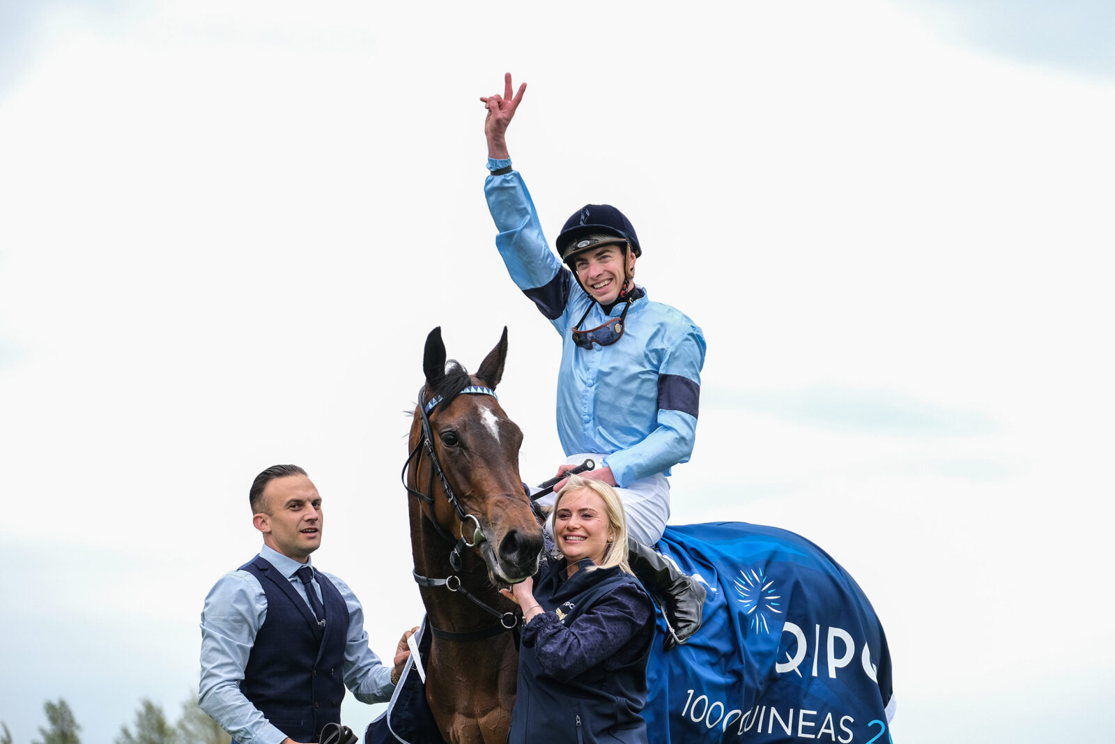 Jockey in blue silks on a racehorse, with two people in foreground